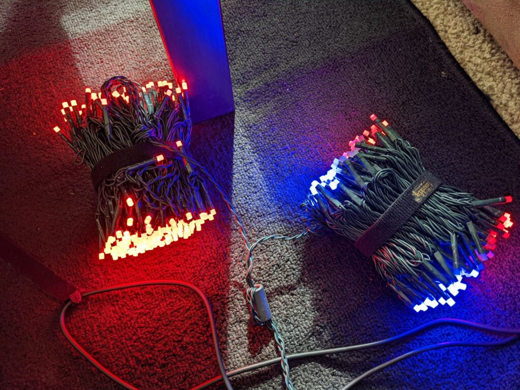 An aerial photo of two packs of wrapped multi-color Christmas lights placed on the ground in blue and red.