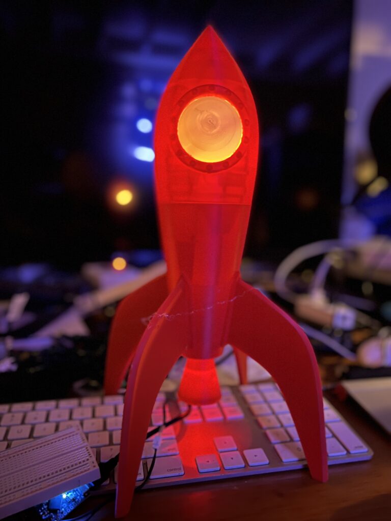 A close up image of a 3D printed red rocket ship sitting on a desk.