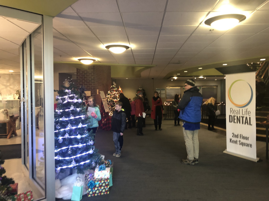 Group of people gathered around in line at an office lobby waiting to interact with a color-changing tree Christmas tree.