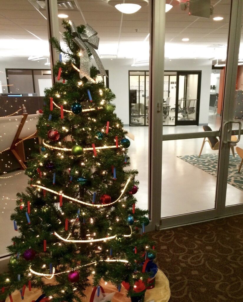 A decorated Christmas tree sitting in front of an indoor office building window. 